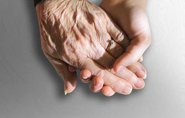 Elderly person's hand holding a younger person's hand
