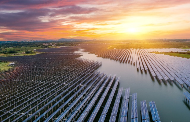 A sunset is pictured with a river in the foreground with a number of solar panels