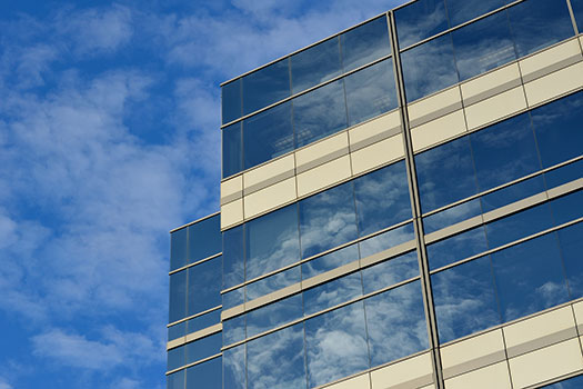 A glass fronted office building reflecting a blue and slightly cloudy sky with similar sky as a backdrop