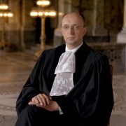 A picture of Judge Peter Tomka he is seated with his hands in his lap and is wearing court dress.