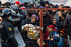 Refugees behind a fence with Croatian police standing guard