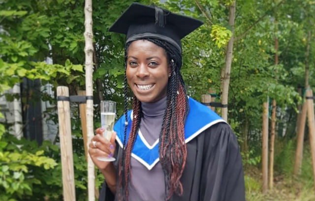 Christine Ohuruogu stands in graduation gown and cap holding her a glass of champagne. She has dark skin and long black and auburn braids.