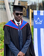 Umar Geidman standing outside Queen's Building in graduation robes
