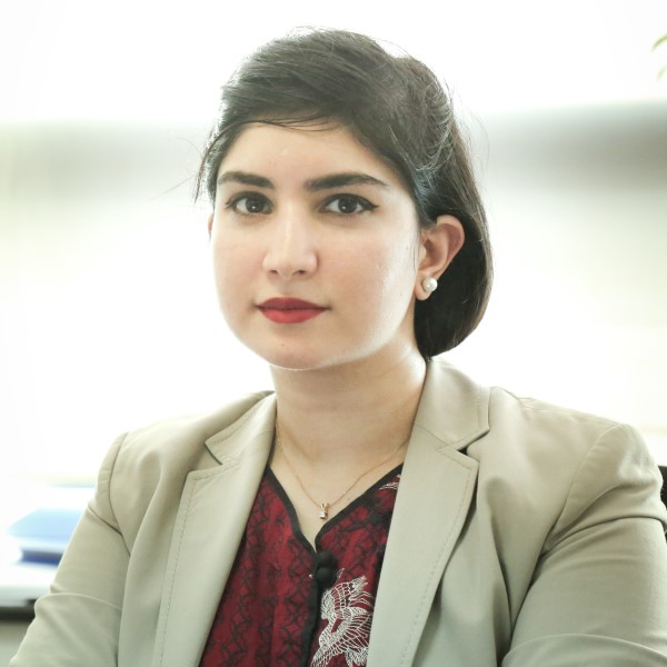 Headshot of alumna, Maha Kamal. She is wearing a beige blazer and burgundy top and her hair is swept back in a formal hairstyle.