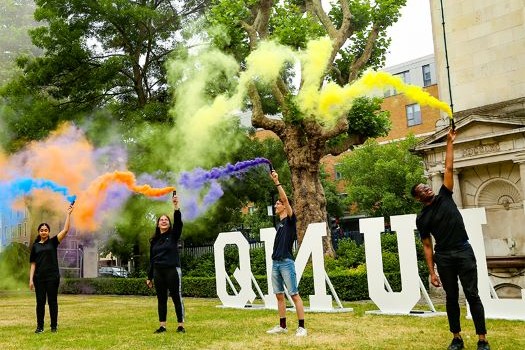 Students with coloured flares in front of QMUL giant letters