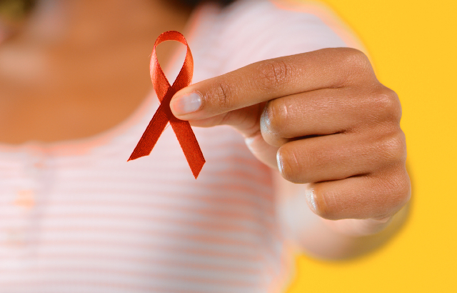 Woman holding up a red ribbon, the universal symbol of awareness and support for people living with HIV. Credit: katleho Seisa/iStock.com