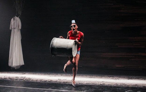 A performer dances carrying a large metal rubbish bin