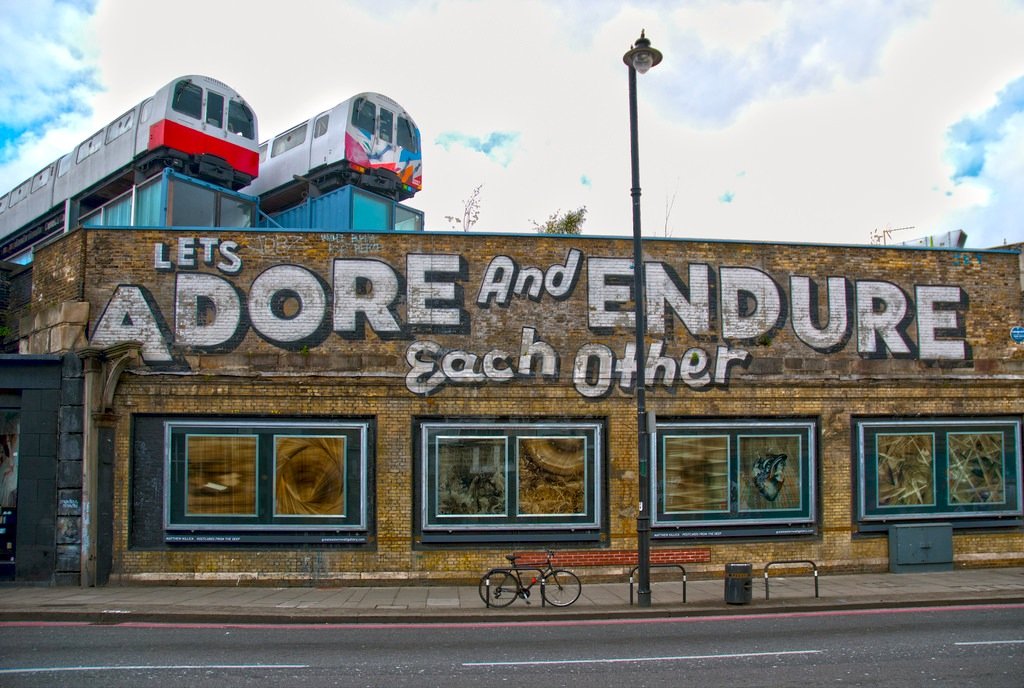 a building in East London with street art on it and two tube train carriages positioned above it