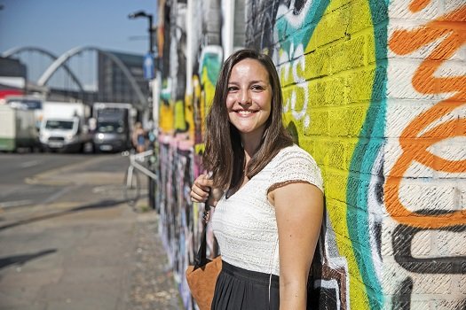 a young woman standing in front of a brightly decorated wall in the East End of London as an example of East End street art