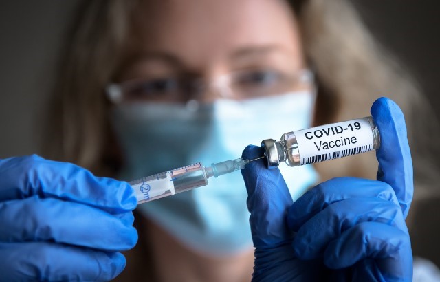 A nurse wearing mask and gloves fills up a syringe from a vial of COVID-19 vaccine.