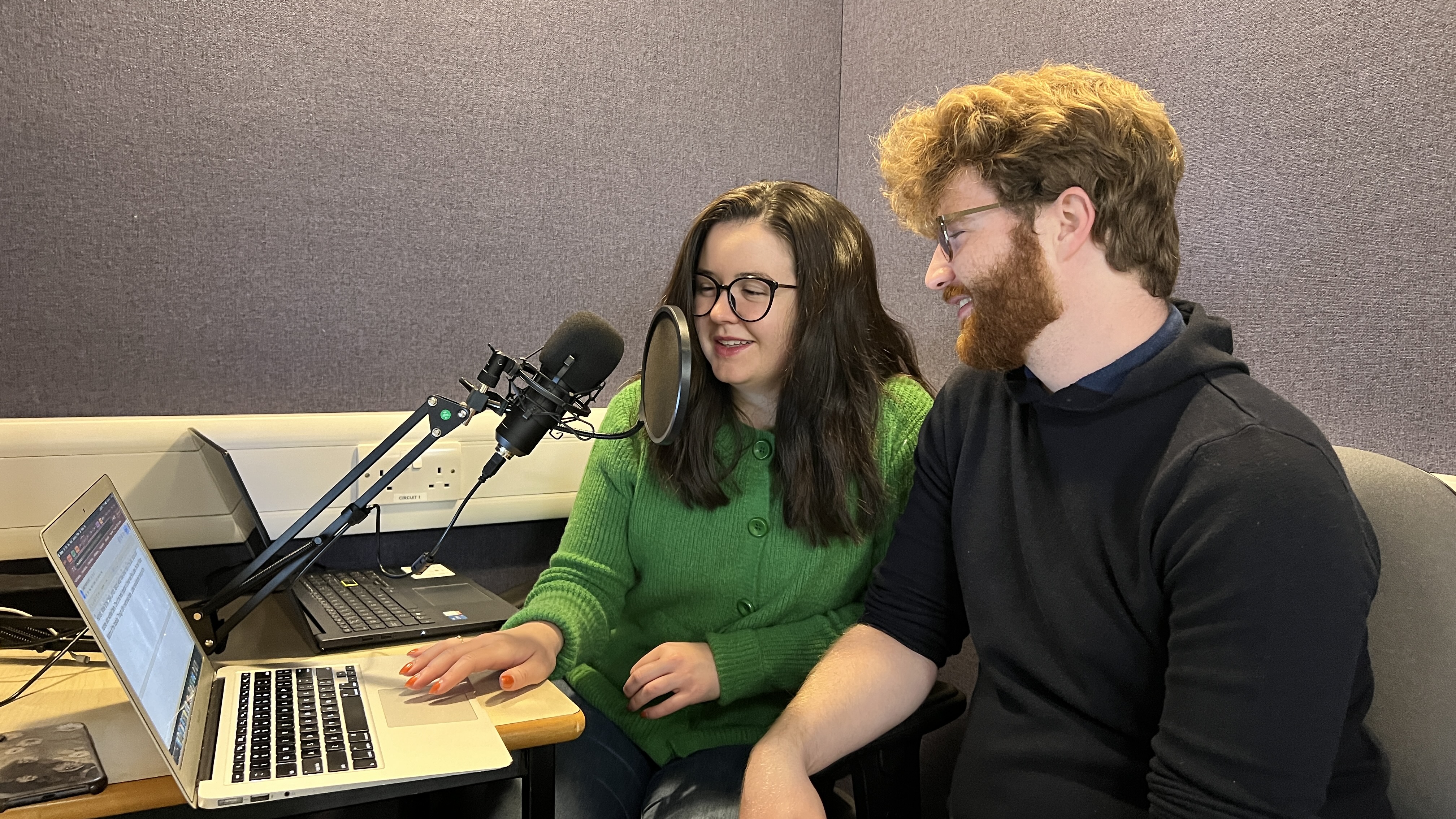 Mary and Hamish talking into a microphone recording their podcast