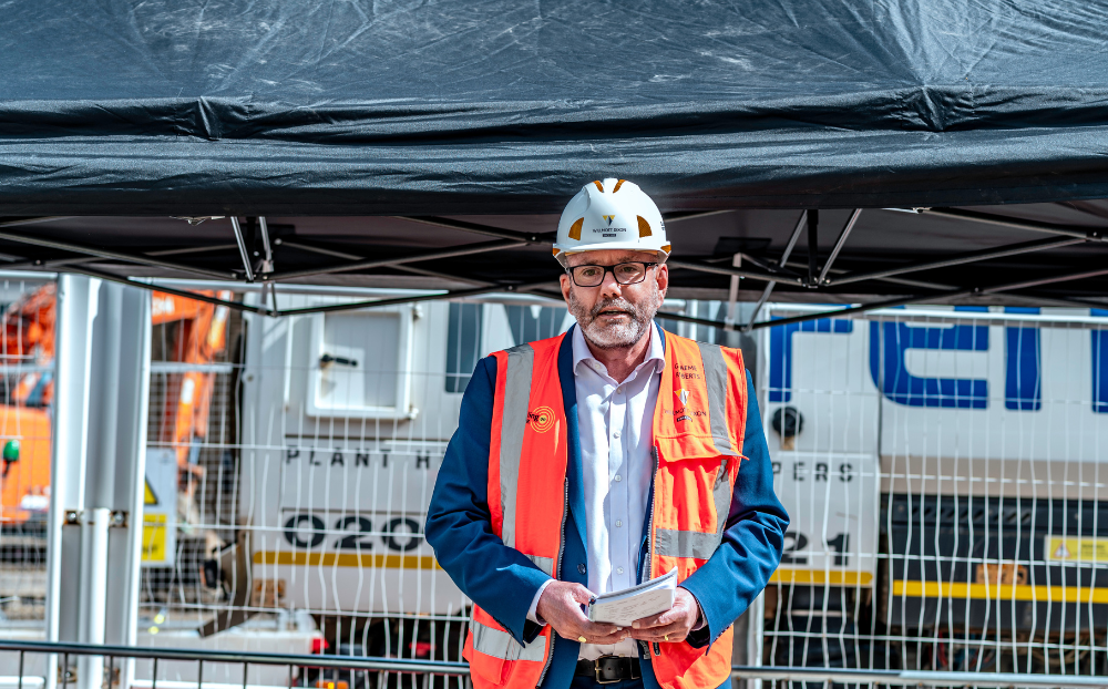 A man with a hard hat on giving a speech at the construction site of the new school of business and management building