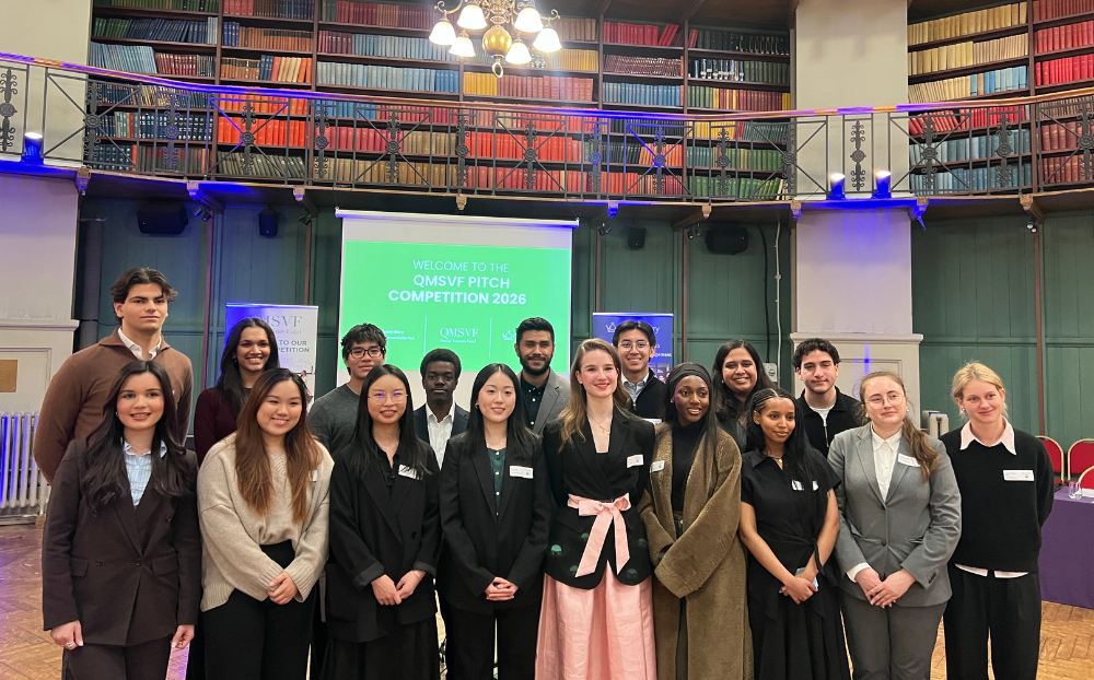 An image of a large group of people standing and smiling infront of a powerpoint in a large hall