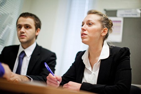 A woman and a man both in smart clothing at a desk taking notes