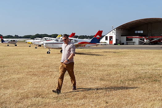 Matthew Gream walking through an air field with planes behind him