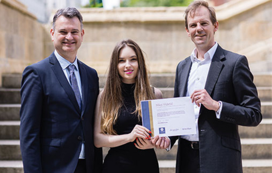 Young woman being handed a certificate award by two men.