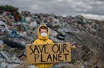 A person holding a sign saying 'save our planet' in a dump full of rubbish