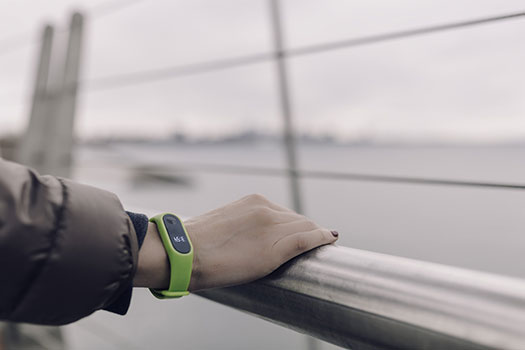Runner's hand leaning on a metal railing wearing a lime green smart watch