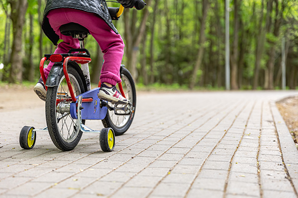 Child rides away from the camera on a bicycle with stabilisers, along a path with trees in the background