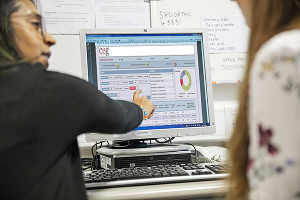 Two healthcare workers point at aspects of a CEG dashboard on their computer screen