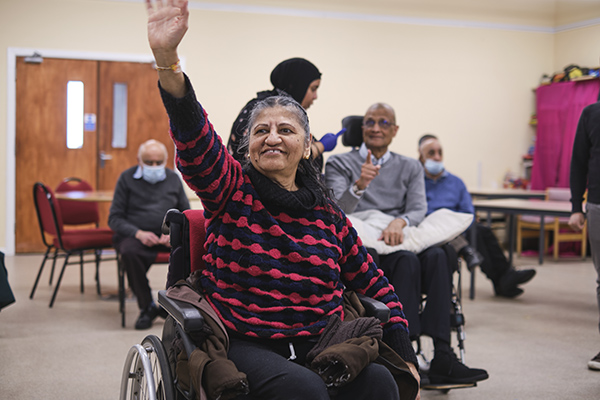 An older woman raises her hand as part of an activity in a community centre
