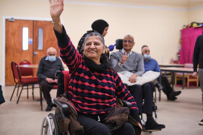An older woman raising her hand, participating in an activity at a community centre