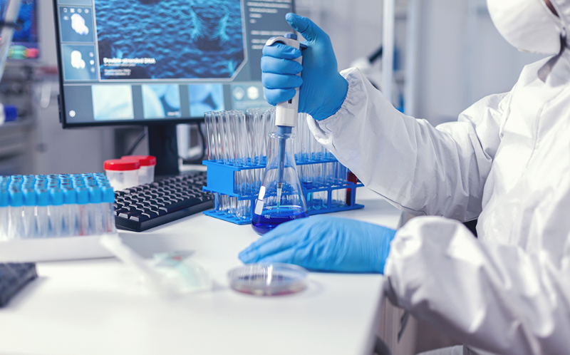 A medical professional in protective lab clothing taking samples of a solution using a pipette.