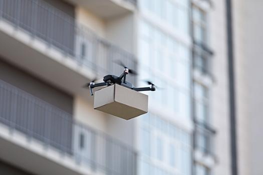 A drone flying by an apartment building with a small package.