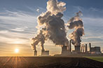 Smoke rising from cooling towers at a German coal-fired power station. It is dawn and the power station is by some fields.