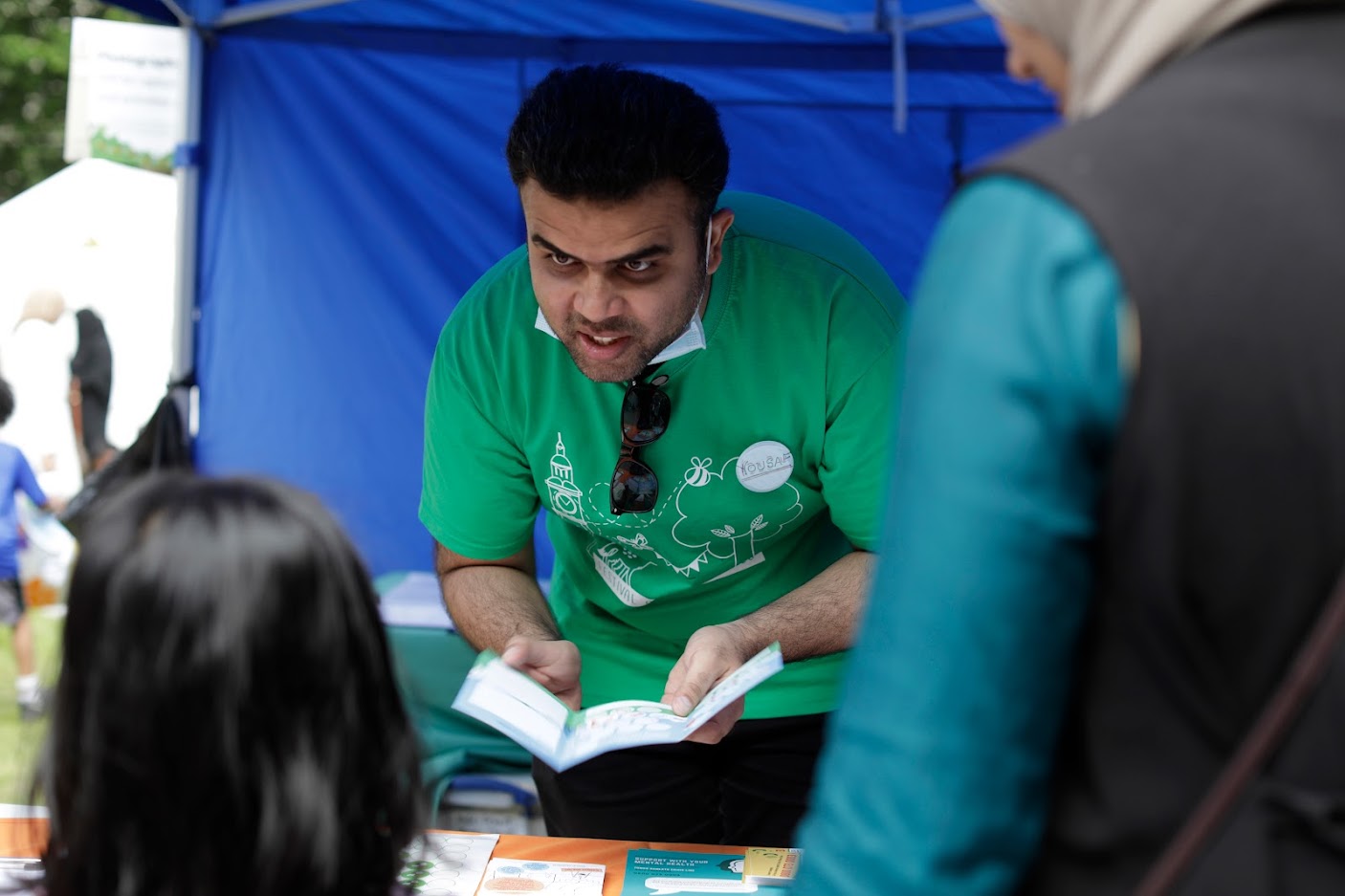 A young man wearing a green Festival T-shirt shows an information leaflet to a child and their grown up
