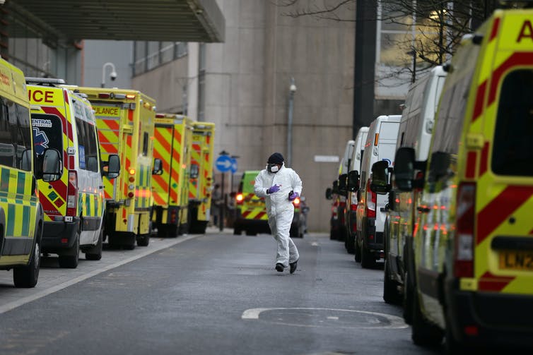 A healthcare worker running along a road where multiple ambulances are parked