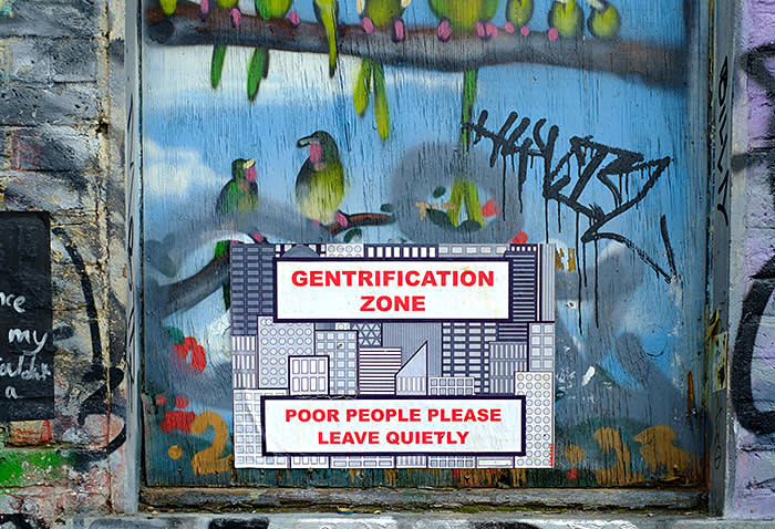 A graphical representation of a city with the labels 'Gentrification Zone' and 'Poor People Please Leave Quietly' are stuck over a painted wall. the wall is painted with green and pink birds that have been painted onto wall, and over the wall and around the sign are graffitti tags in black and grey.
