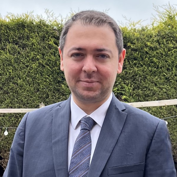 Headshot of alumnus, Nizamettin Dogan Guner. He is standing in a garden wearing a suit and tie.