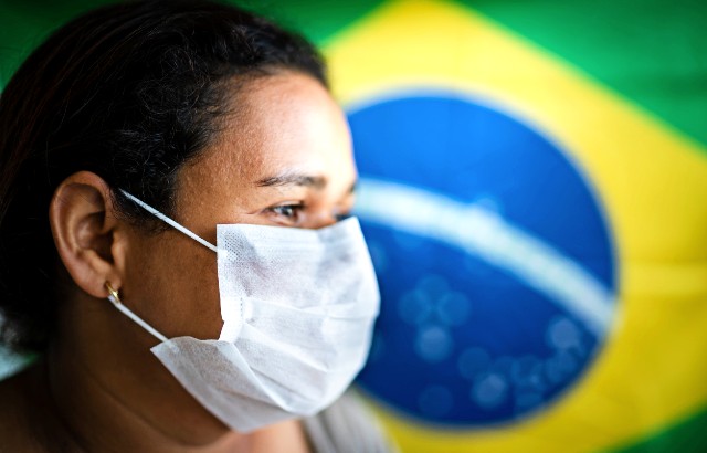 A woman wearing a face covering in front of a Brazilian flag