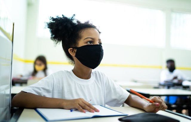A schoolgirl wearing a face covering studies in a classroom