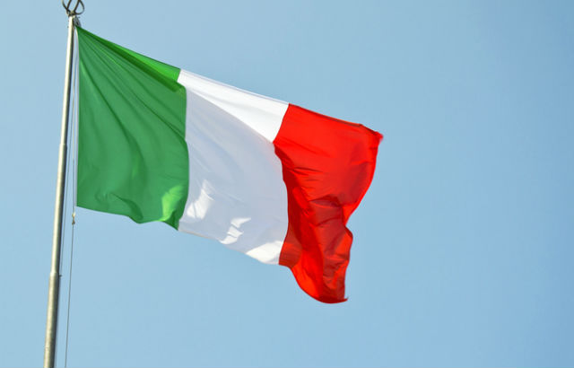 An Italian flag with bands of green, white and red set against a clear blue sky