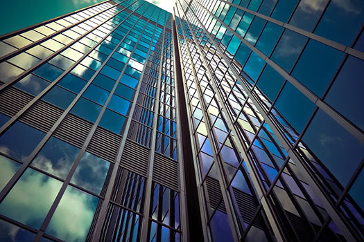 View of a glass office building from the ground up with the cloudy blue sky reflected on the surface