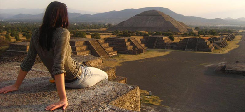 A student outside admiring a national ancient monument against a sunset.