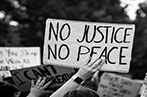 Greyscale image of someone holding up a sign saying 'no justice, no peace' at a protest. Another sign in front says 'I can't breathe'.