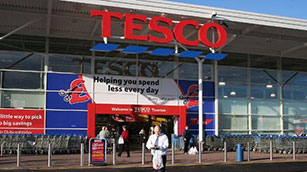 Front of a Tesco Superstore with man walking with a shopping bag through the car park