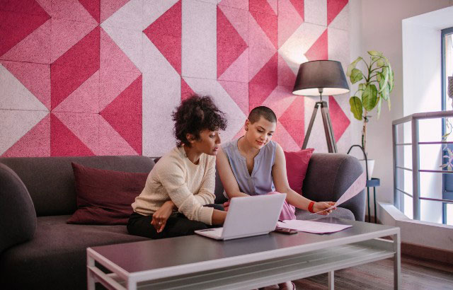 A black woman and a white woman sat in office with pink patterned wall paper