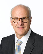 Charles Randell in glasses, a suit and blue and gold spotted tie
