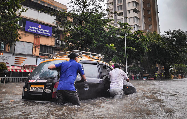 Two men pushing a black car through flood waters