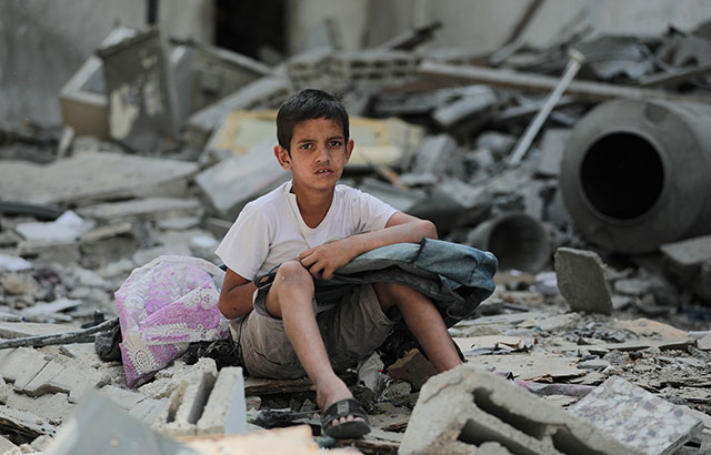 A child in Gaza sitting on the rubble of destroyed buildings.