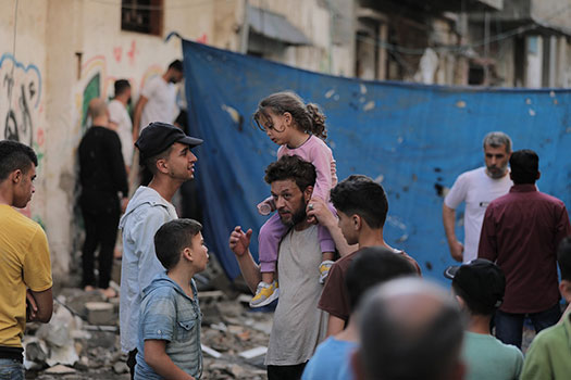 An adult and children looking upset around rubble in Gaza.