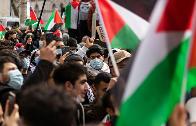 A protest for Palestine in London, with people wearing masks and holding Palestinian flags.