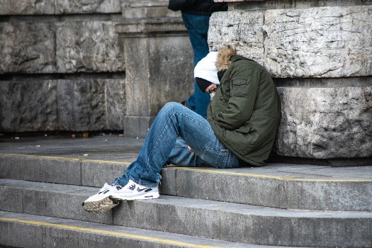 Homeless person sat on the steps of a building huddling up from the cold
