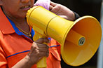 A person wearing an orange coat using a yellow megaphone. Their face is largely obscured.