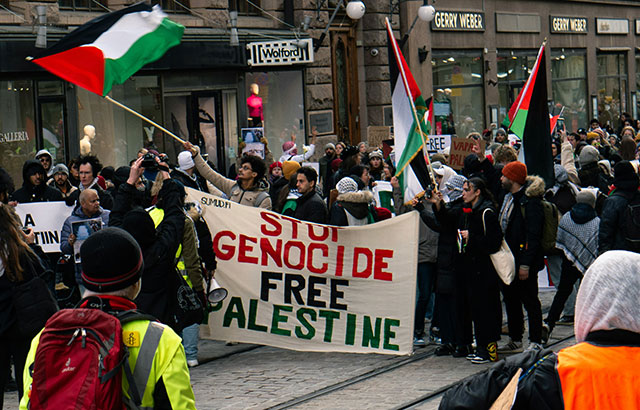 A group of protesters holding a sign saying 'STOP GENOCIDE FREE GAZA'.