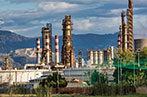 An oil refinery with various chimneys. There are mountains in the background.